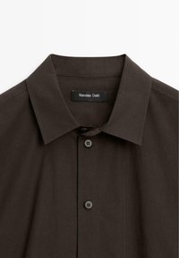 Chemise à boutons marron foncé avec un col italien et deux boutons visibles, portant une étiquette Massimo Dutti à l'intérieur du col.