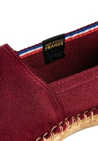 Chaussure en tissu bordeaux avec semelle en jute tissée, comportant une étiquette noire marquée "FABRIQUÉ À SOULE, FRANCE" et des accents de couture rouge, blanc et bleu.