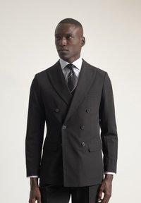 Chaqueta de traje negra de doble botonadura con solapas de muesca, camisa de vestir blanca a rayas y corbata negra lisa. Presenta un corte ajustado y un diseño elegante.