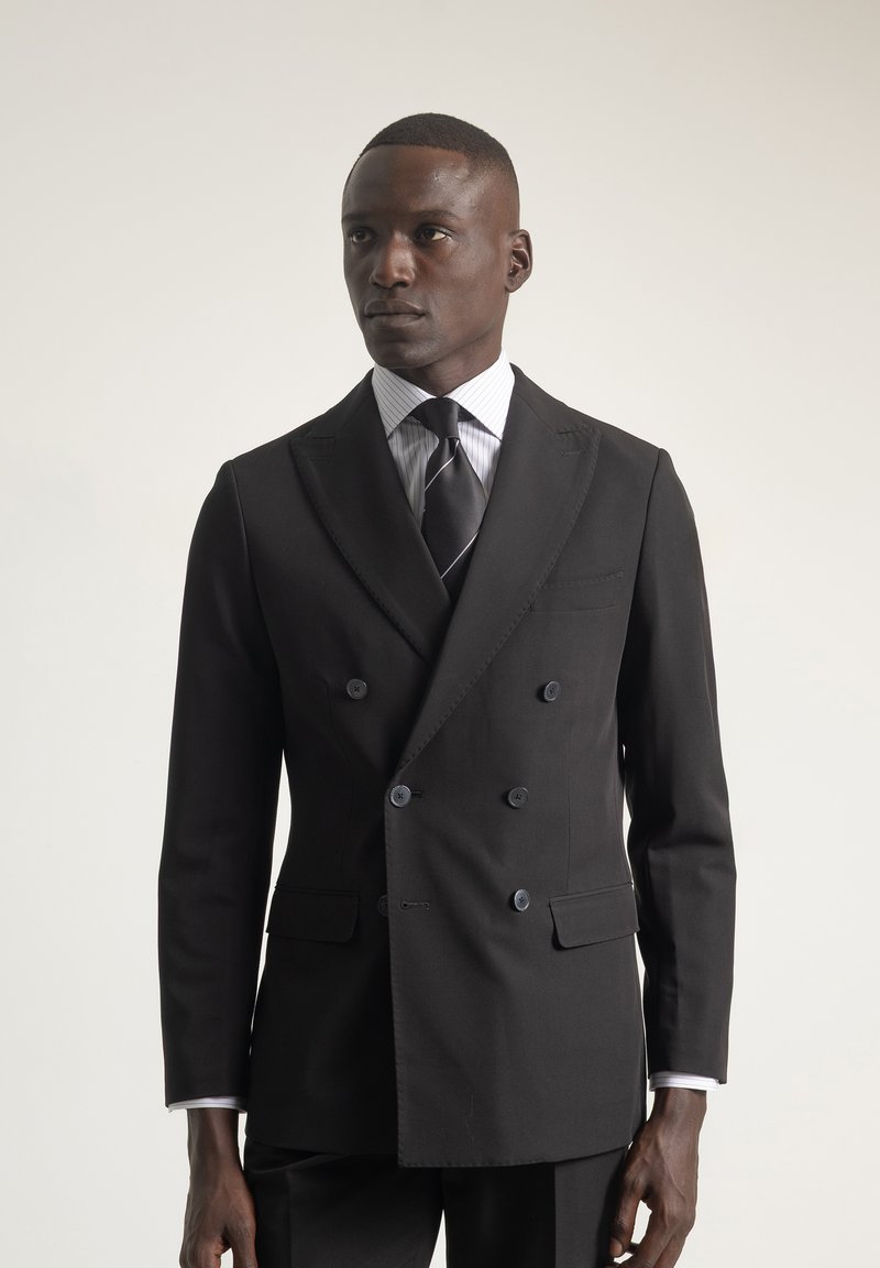 Chaqueta de traje negra de doble botonadura con solapas de muesca, camisa de vestir blanca a rayas y corbata negra lisa. Presenta un corte ajustado y un diseño elegante.