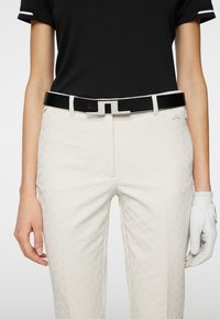 Black belt with a silver rectangular buckle, paired with light beige textured pants. Light black shirt with white accents. White golf glove on hand.