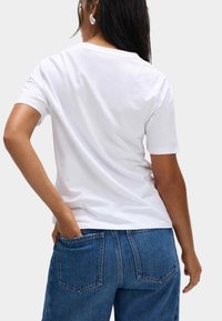 Bílý bavlněný tričko s kulatým výstřihem, krátkými rukávy a hladkou strukturou; kombinováno s modrými džíny s vysokým pasem a zadními kapsami.
