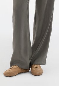 Pantalons gris à jambes larges associés à des baskets en daim beige avec un tissu texturé et des lacets doux, mettant en valeur une coupe décontractée et un design casual.