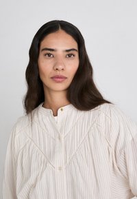 Cream, striped blouse with a mandarin collar, button detail, and gathered fabric for a relaxed fit. Soft texture, casual design.