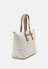 Beige stoffen draagtas met een gestructureerd oppervlak, dubbele bruine handvatten en een ritssluiting. Voorzien van geometrische stiksels voor extra detail.