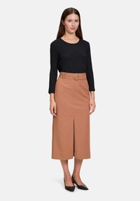 Zwart gestructureerd langsliefhemd gecombineerd met een taupe midi-jurk met een split aan de voorkant en een ceintuur in de taille. Zwarte puntige hakken maken de look compleet.