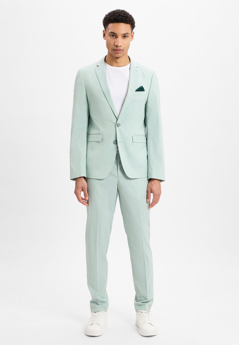 Helle mintgrüne Anzugjacke mit einem einreihigen Schnitt, Revers und zwei Vordertaschen. Kombiniert mit einem weißen T-Shirt und weißen Sneakern.