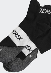 Calcetines deportivos negros y grises con una banda superior acanalada, que presentan el logotipo "TERREX" en blanco, y un talón y puntera reforzados para mayor durabilidad.