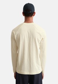 Cremefarbenes Langarmshirt mit Raglanärmeln. Weiche Textur, runder Halsausschnitt und lässige Passform. Getragen mit einer schwarzen Mütze, von hinten gezeigt.