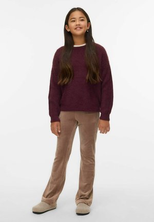 Bordos krāsas pūkains džemperis, bēša samta bikses un pelēkas čības. Džemperim ir gari piedurkņu gali un brīvs piegriezums, bikses ir platām kājām.