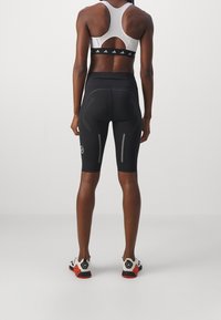 Pantaloncini da ciclismo neri con dettagli riflettenti e design aderente, abbinati a un reggiseno sportivo grigio con schiena traforata e fascia elastica.