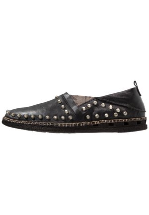 Scarpa slip-on in pelle nera con borchie rotonde d'argento, suola cucita e linguetta al tallone, mostrata su sfondo bianco.