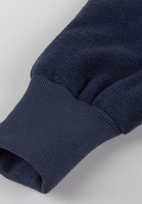 Dunkelblauer Pulloverärmel mit Fleece-Struktur und gerippten Bündchen. Der Stoff wirkt weich und warm, ideal für die Freizeit.