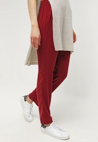 Red loose-fitting trousers made of soft fabric, featuring an elastic waistband and side pockets, paired with white sneakers.