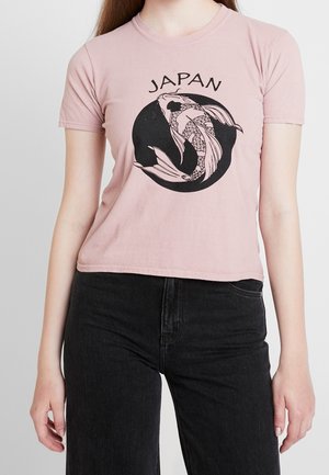Woman wearing light pink cropped T-shirt with black koi fish design and "JAPAN" text, paired with high-waisted black jeans.