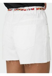 Beli kavbojke iz bele denima s frayed robom, ki imajo zadnje žepe in večbarven pleten pas v pasu.