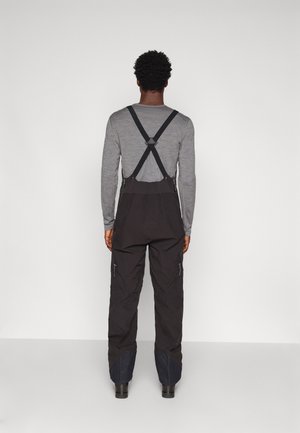 Salopettes noires imperméables avec des bretelles réglables, dotées de poches zippées sur les côtés et d'accents en tissu contrastant au niveau des chevilles.