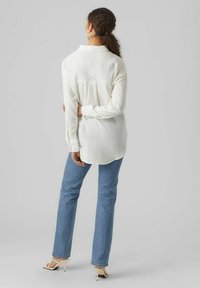 White textured long-sleeve shirt, relaxed fit, buttoned cuffs; paired with light blue high-waisted jeans and white heeled sandals.