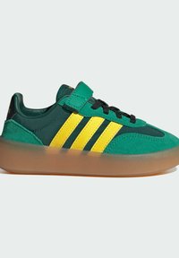 Gröna mockasneakers med gula ränder och svarta snören. Har en vadderad plös och en genomskinlig gummisula. Välcrorem medföljer.