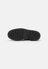 Semelle en caoutchouc noir avec de profondes rainures et un motif strié, présentant des encoches en forme de croix pour une traction et une durabilité optimales.
