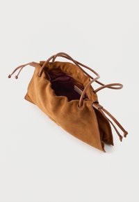 Sac à cordon en daim marron avec une texture douce, haut froncé et poignées en cuir marron. L'intérieur est doublé d'un tissu bordeaux profond.