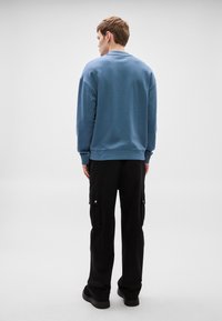 Βαμβακερό φούτερ με στρογγυλή λαιμόκοψη σε απαλό μπλε, με χαλαρή εφαρμογή και ριμπ μανσέτες. Συνδυάζεται με μαύρο παντελόνι cargo και μαύρα παπούτσια.