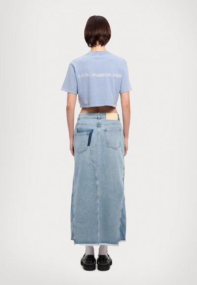 Cropped light blue t-shirt with “HOLZWEILER” printed on the back, paired with a long, light blue denim skirt featuring pockets and raw hem.