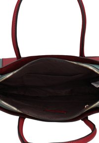 Sac à main ouvert présentant un extérieur en cuir rouge et sarcelle, une fermeture éclair noire et un intérieur en tissu marron avec une poche plate.