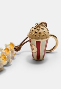 Portachiavi a forma di secchiello di popcorn dorato con strisce rosse e bianche, coperchio a cupola texturizzato e cordino marrone. Include un piccolo dettaglio di popcorn accanto.