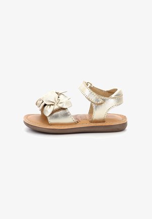 Sandalia de cuero metálico dorado con detalle de lazo, punta abierta y correa ajustable para el tobillo. Suela marrón y forro interior.