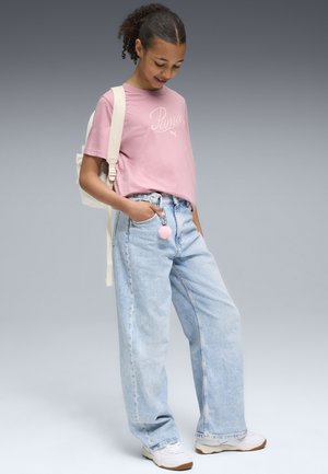 T-shirt en coton rose avec le logo "Puma", jean en denim large à lavage léger, baskets blanches et un sac à dos crème avec un pompon rose.