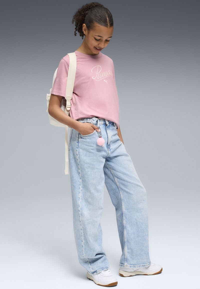 T-shirt en coton rose avec le logo "Puma", jean en denim large à lavage léger, baskets blanches et un sac à dos crème avec un pompon rose.