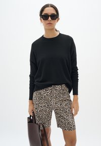 Un pull noir à manches longues, un short à motif léopard et un sac fourre-tout marron foncé. Des lunettes de soleil avec une forme distinctive en œil de chat.