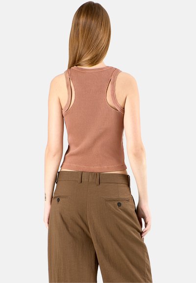 Rostfarbener gerippter Tanktop mit weiten Armöffnungen und rundem Halsausschnitt, kombiniert mit hochgeschnittenen, braunen weit geschnittenen Hosen mit Gesäßtaschen.