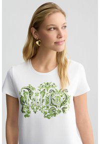 T-shirt en coton blanc avec un motif floral et orné vert, arborant le nom de la marque "Liu Jo" en lettres embellies.