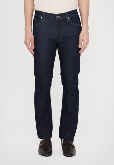 Dunkelblaue Jeans aus Denim mit geradem Schnitt, ausgestattet mit goldenen Nähten, fünf Taschen und einem Knopfverschluss. Glatte Textur mit minimaler Gestaltung.