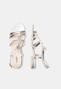 Sandales à lanières avec une finition argent métallique, bout ouvert, quincaillerie florale décorative et un petit talon carré. Semelle intérieure en cuir lisse.