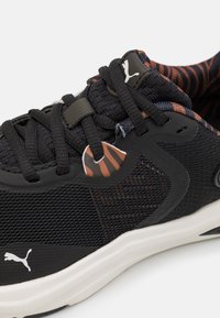 Scarpa da ginnastica nera con tomaia in rete, dettagli in gomma e una fodera interna con motivo testurizzato. Presenta un logo e una suola bianchi a contrasto.