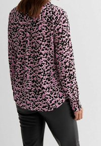 Blusa a maniche lunghe in tessuto rosa con motivo astratto nero e viola, con orlo curvo e dettagli polsini con bottoni.