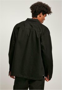 Svart denimskjorte med en avslappet passform, synlige sømmer, og "SOUTHPOLE" brodert på bakre yoke. Myk tekstur med lange ermer.