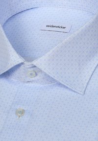 Chemise de costume bleu clair à motifs, avec un col pointu et deux boutons visibles, portant une étiquette de la marque "seidensticker" à l'intérieur du col.