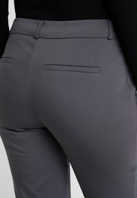 Pantalon gris sur mesure avec un tissu texturé, une finition lisse, des poches arrière et une coupe ajustée.