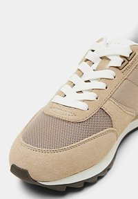 Baskets beige en daim et mesh avec lacets blancs et semelle noire texturée, vues de profil avant.