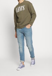 Olivově zelená mikina s bílým nápisem "LEVI'S", doplněná světle modrými džínami a levandulovými teniskami, s ohrnutými manžetami a pohodlným střihem.