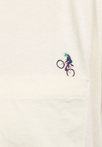 T-Shirt aus Baumwolle in Off-White mit aufgestickter Tasche. Mit gesticktem Grafikdesign eines Radfahrers in Blau und Pink, der vor einem hellen Hintergrund fährt.