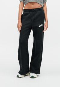 Črne trenirke z elastičnim pasom in vrvico za zategovanje. Na levi stegni je bel logotip Nike. Izdelane iz mehke tkanine.