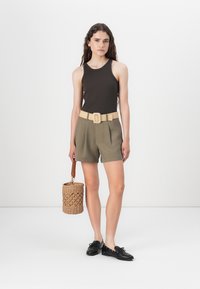 Rudas be rankovių marškinėliai, alyvų žalumo šortai su smėlio spalvos diržu ir juodi batai. Laikanti pintą krepšį su rudais rankenomis.