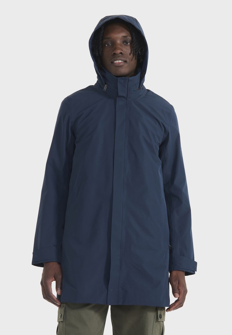 Tamno plava vodootporna jakna s kapuljačom, visokim ovratnikom i dugim rukavima. Karakterizira je glatka tekstura i minimalistički dizajn.