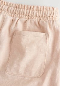 Shorts en tissu rose clair avec taille élastique et une poche arrière unique. Matériau texturé avec un léger éclat et des détails de couture.
