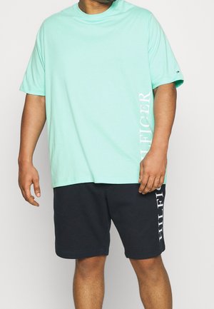 Light green cotton T-shirt with short sleeves, featuring white vertical text on the side; paired with navy shorts displaying similar text.